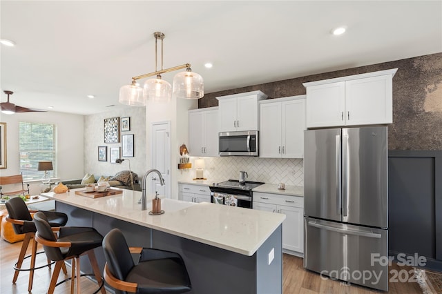 kitchen featuring light hardwood / wood-style flooring, white cabinets, a center island with sink, appliances with stainless steel finishes, and decorative light fixtures