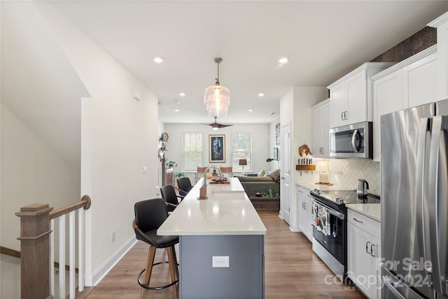 kitchen with light hardwood / wood-style flooring, white cabinets, a kitchen island, and appliances with stainless steel finishes