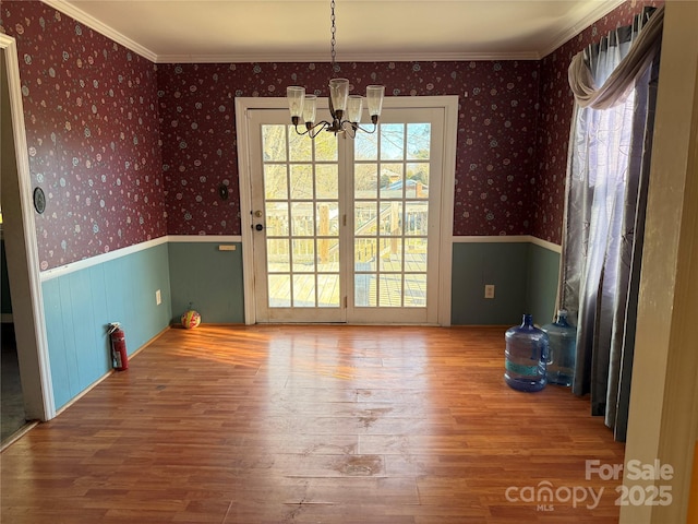 unfurnished dining area featuring wood-type flooring, ornamental molding, and an inviting chandelier