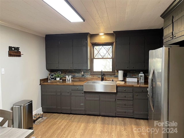 kitchen featuring sink, wood counters, light hardwood / wood-style flooring, stainless steel fridge, and decorative backsplash