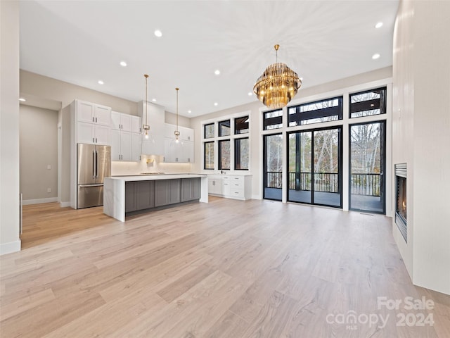 kitchen featuring stainless steel fridge, pendant lighting, a spacious island, white cabinets, and light wood-type flooring