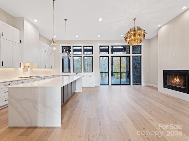 kitchen with light stone countertops, light wood-type flooring, white cabinets, hanging light fixtures, and a large island