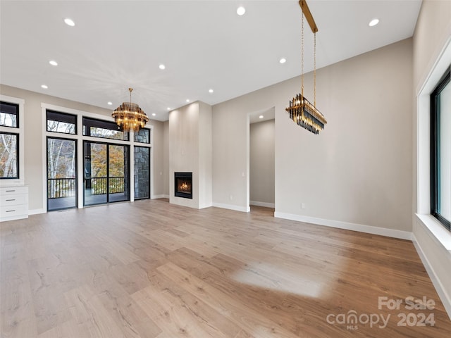 unfurnished living room featuring a large fireplace, light hardwood / wood-style flooring, and a chandelier