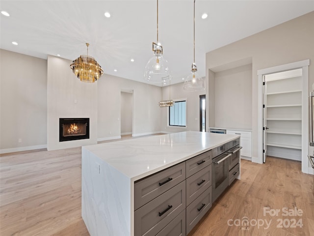 kitchen with light hardwood / wood-style flooring, a kitchen island, pendant lighting, a large fireplace, and light stone countertops