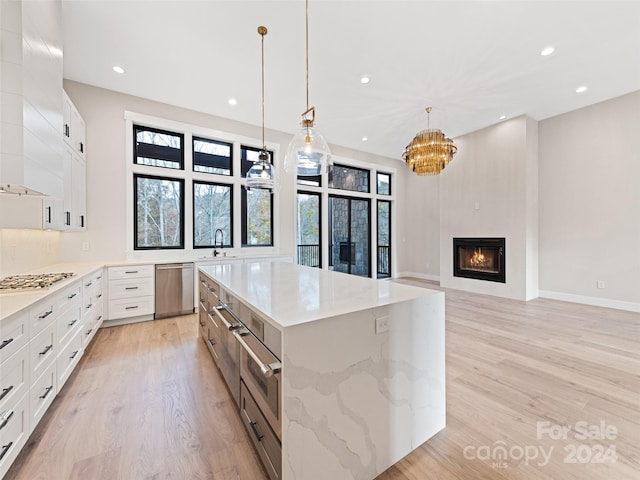 kitchen with light stone countertops, stainless steel appliances, decorative light fixtures, light hardwood / wood-style flooring, and white cabinets