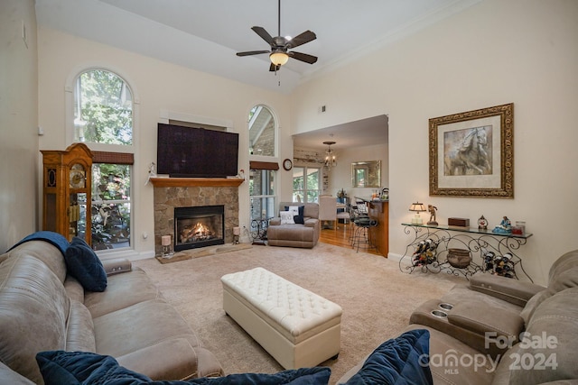 carpeted living room with ceiling fan, a healthy amount of sunlight, a stone fireplace, and high vaulted ceiling