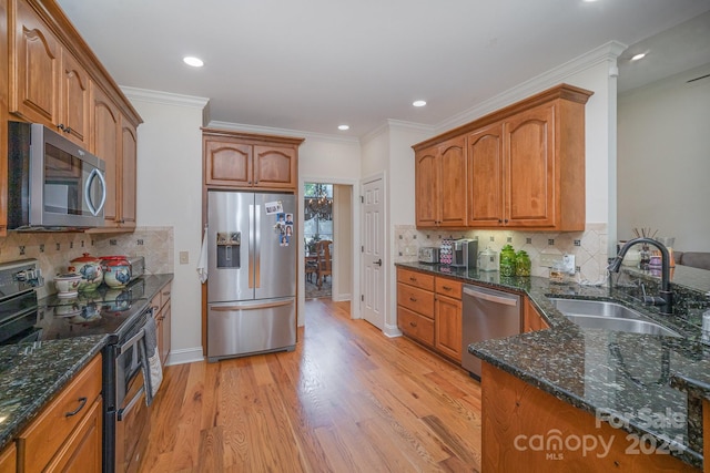 kitchen with sink, stainless steel appliances, dark stone countertops, decorative backsplash, and light wood-type flooring