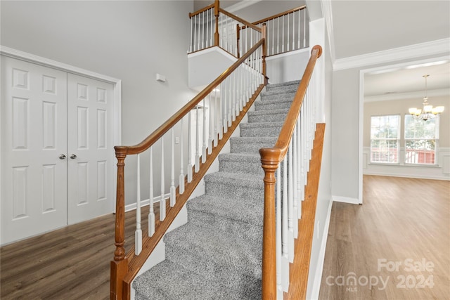 stairs with a chandelier, wood-type flooring, and ornamental molding