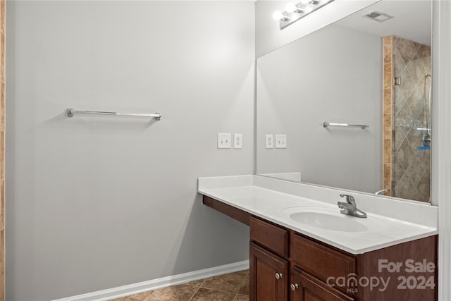 bathroom featuring tile patterned flooring, a tile shower, and vanity