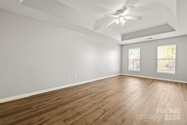 empty room featuring a raised ceiling, ceiling fan, and wood-type flooring