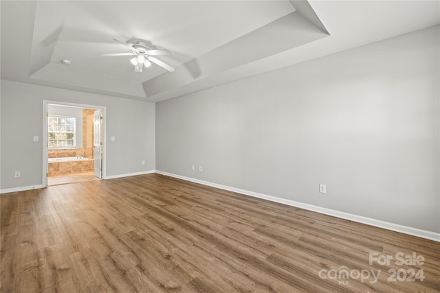 empty room with a tray ceiling, ceiling fan, and light hardwood / wood-style floors