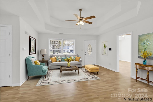 living room with ceiling fan, light hardwood / wood-style floors, and a tray ceiling