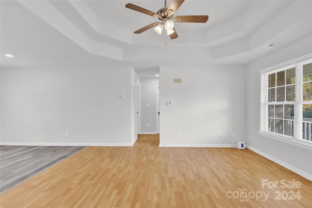 spare room with a tray ceiling, ceiling fan, and light wood-type flooring