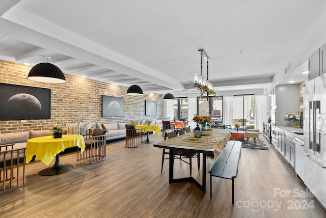 dining area featuring hardwood / wood-style flooring, beamed ceiling, brick wall, and a chandelier