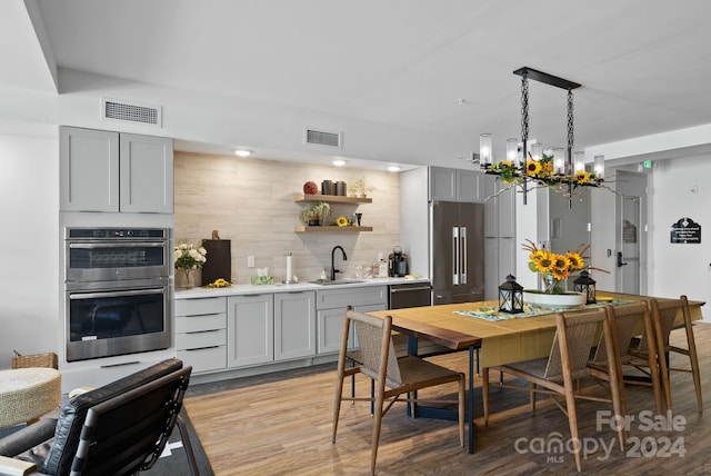 kitchen featuring appliances with stainless steel finishes, decorative light fixtures, light hardwood / wood-style flooring, a notable chandelier, and gray cabinets