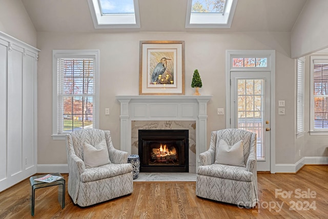 living area with hardwood / wood-style floors, lofted ceiling with skylight, and a high end fireplace