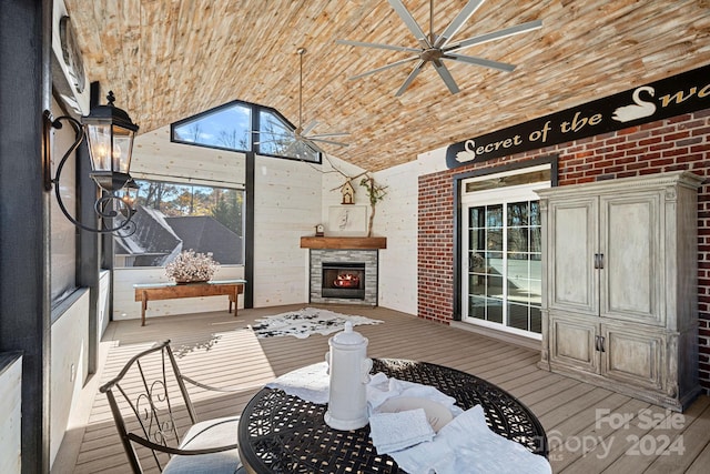 sunroom with ceiling fan, a stone fireplace, and lofted ceiling