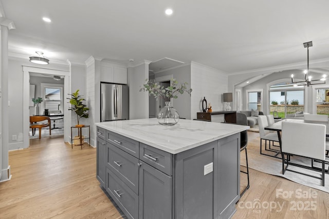 kitchen featuring a kitchen island, stainless steel fridge, hanging light fixtures, light stone counters, and light wood-type flooring