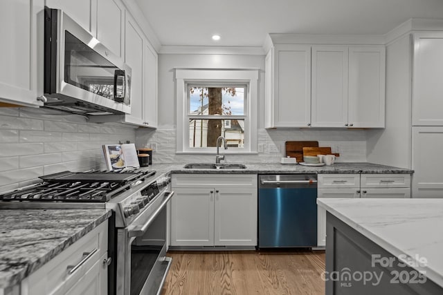 kitchen with sink, appliances with stainless steel finishes, white cabinetry, light stone counters, and light wood-type flooring