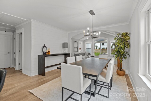 dining space with ornamental molding, vaulted ceiling, an inviting chandelier, and light hardwood / wood-style floors