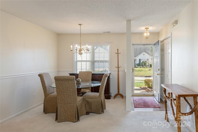 dining area with a textured ceiling, a healthy amount of sunlight, light carpet, and an inviting chandelier