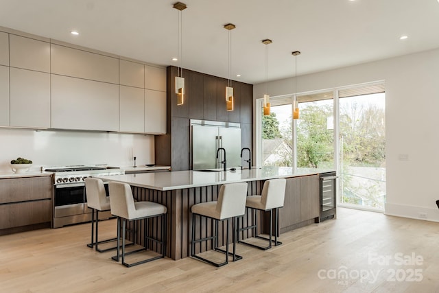 kitchen with wine cooler, high end appliances, decorative light fixtures, a kitchen breakfast bar, and light hardwood / wood-style floors