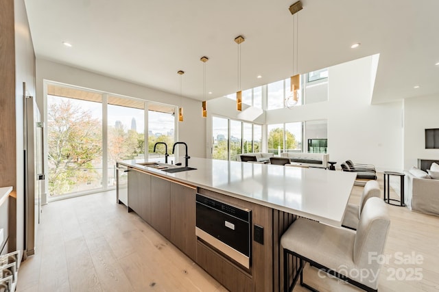 kitchen with a spacious island, sink, hanging light fixtures, stainless steel dishwasher, and light hardwood / wood-style floors