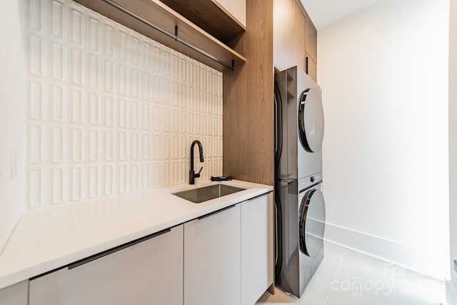 clothes washing area featuring cabinets, stacked washer and clothes dryer, sink, and light tile patterned floors