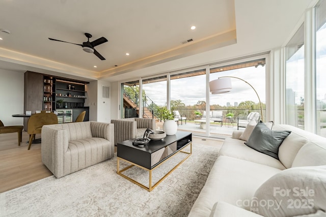 living room featuring ceiling fan, indoor bar, a tray ceiling, and light hardwood / wood-style floors