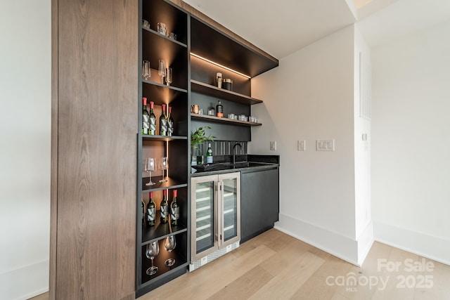 bar with sink, beverage cooler, and light wood-type flooring