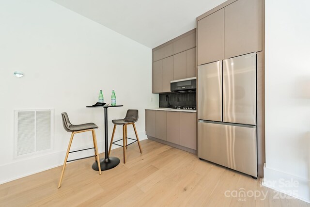 kitchen featuring light hardwood / wood-style floors, gray cabinets, black appliances, and a breakfast bar area