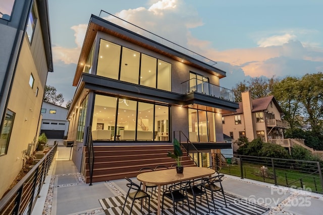 back house at dusk featuring a balcony and a patio