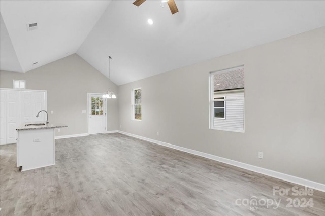 unfurnished living room with sink, high vaulted ceiling, light hardwood / wood-style floors, and ceiling fan with notable chandelier