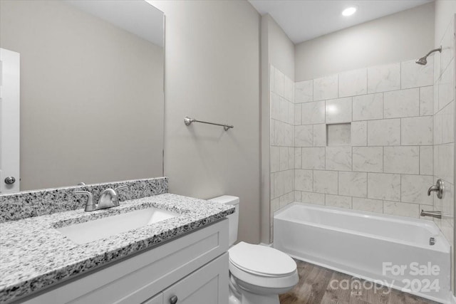 full bathroom featuring vanity, tiled shower / bath combo, hardwood / wood-style flooring, and toilet