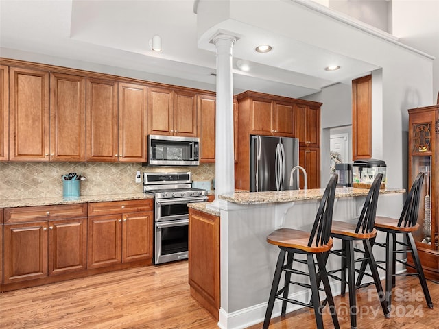 kitchen featuring a kitchen bar, light wood-type flooring, ornate columns, light stone counters, and stainless steel appliances