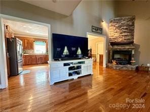 living room featuring a stone fireplace, lofted ceiling, and light hardwood / wood-style flooring