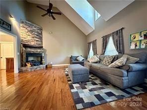 living room with a skylight, wood-type flooring, high vaulted ceiling, a fireplace, and plenty of natural light