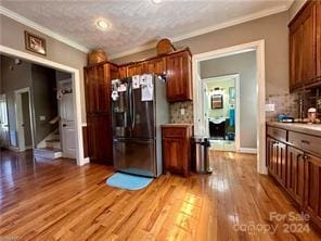 kitchen featuring crown molding, stainless steel fridge, a textured ceiling, tasteful backsplash, and light hardwood / wood-style floors