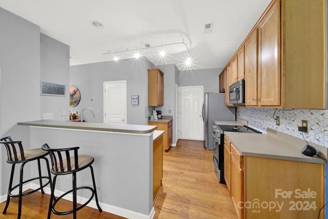 kitchen featuring kitchen peninsula, track lighting, a breakfast bar, stainless steel appliances, and light hardwood / wood-style floors