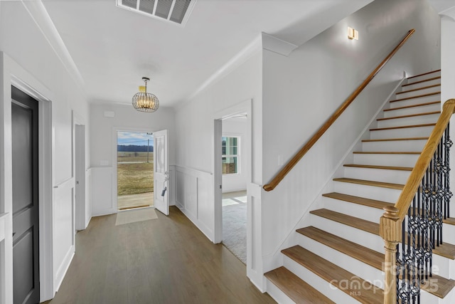 foyer entrance with wood-type flooring, crown molding, and an inviting chandelier