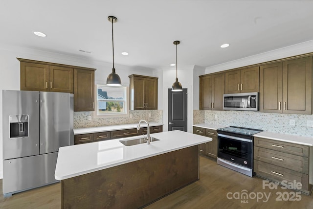 kitchen featuring decorative light fixtures, sink, ornamental molding, stainless steel appliances, and a center island with sink