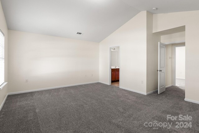 unfurnished bedroom featuring high vaulted ceiling, ensuite bathroom, dark carpet, and multiple windows