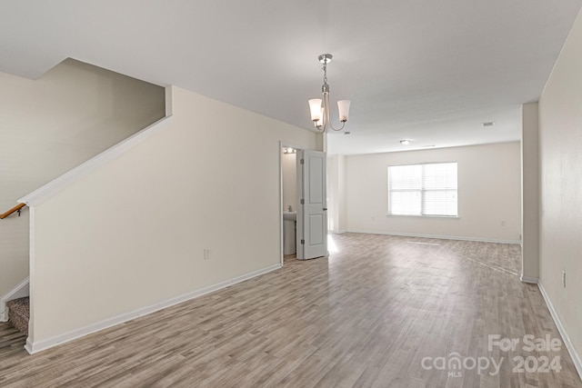 unfurnished room with a chandelier and light wood-type flooring