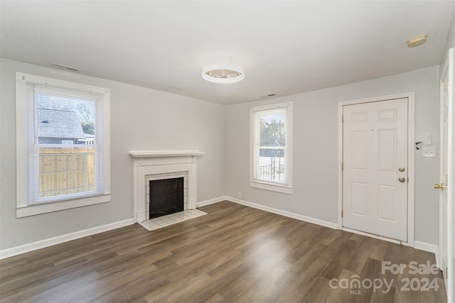 unfurnished living room with a tile fireplace, dark hardwood / wood-style floors, and a wealth of natural light