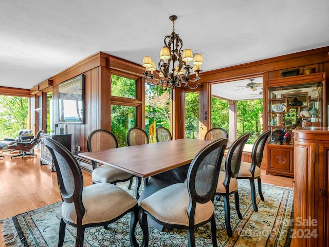 dining room with wooden walls, light hardwood / wood-style flooring, and ceiling fan with notable chandelier