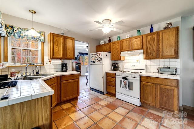 kitchen featuring tile countertops, sink, pendant lighting, tasteful backsplash, and white appliances