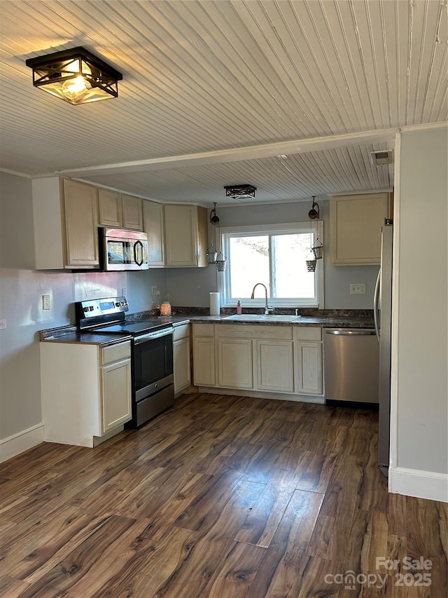 kitchen featuring dark wood-style floors, cream cabinetry, stainless steel appliances, dark countertops, and a sink