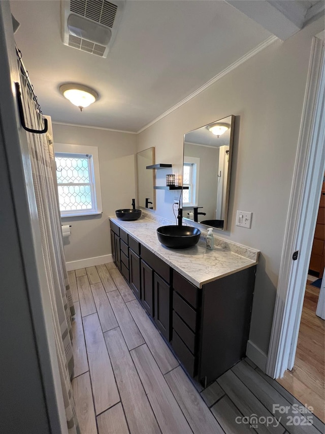 full bathroom with a sink, visible vents, wood tiled floor, double vanity, and crown molding