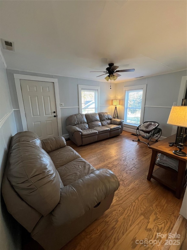 living room featuring a ceiling fan, visible vents, ornamental molding, and wood finished floors