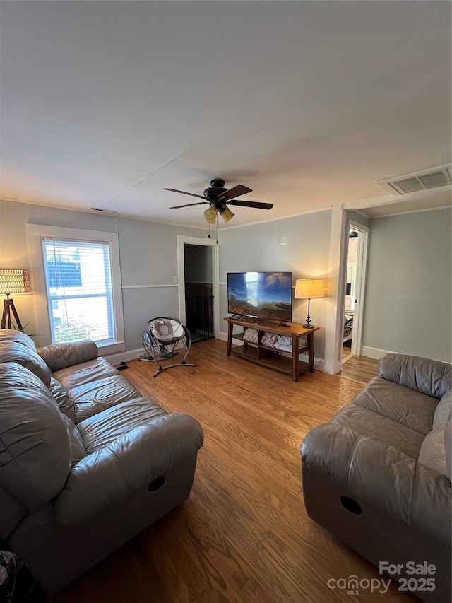 living room featuring light wood-style floors, baseboards, visible vents, and a ceiling fan